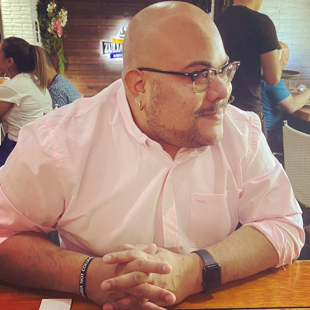 Alberto Rojas smiling in a red plaid shirt and tortoise shell glasses